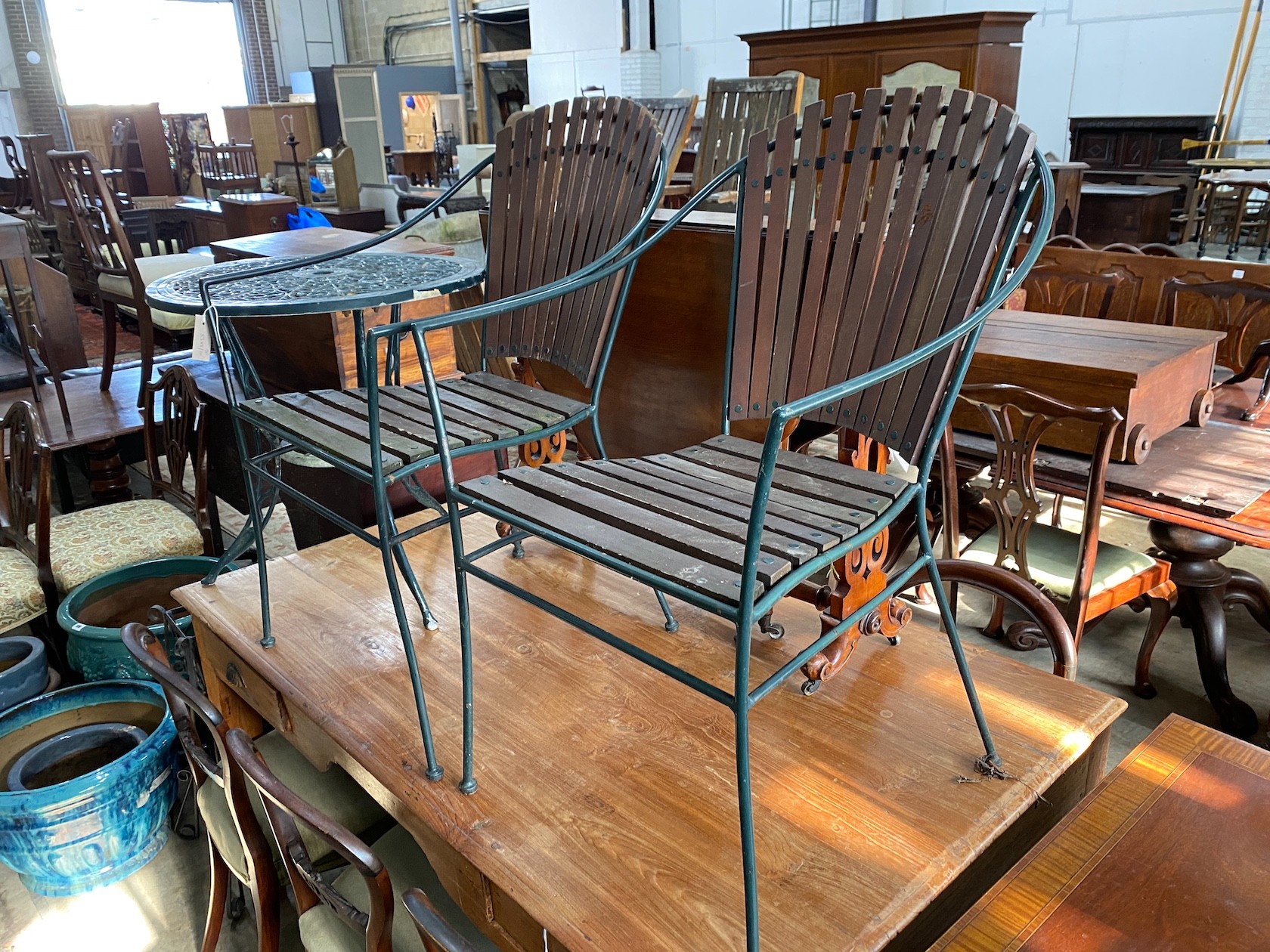 Two wrought iron slatted garden chairs, a circular table and a wrought iron pot stand